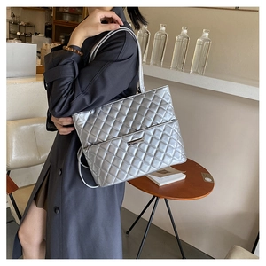 Detail of silver quilted tote bag with metallic finish and rectangular metal logo plate