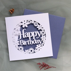 Macro detail of laser-cut daisy flower birthday card with elegant pearlescent blue envelope