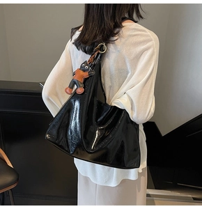 Detail view of glossy black tote bag with cute cat charm and high-shine leather texture
