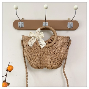 Detail of handmade woven straw bag with circular handles, lace bow and rustic shoulder strap