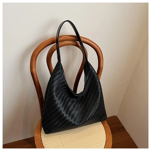Close-up of black woven leather shoulder bag with chevron texture on a wooden chair