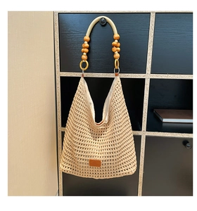 Detailed close-up of hollow knit tote bag with wooden bead straps and leather logo patch