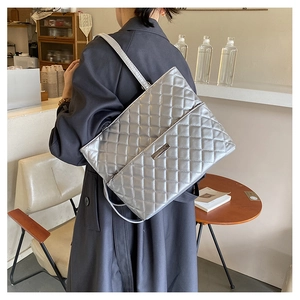 Silver quilted shoulder bag with metal plate detail and chain strap in cafe setting