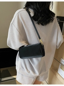 Minimalist black cylinder shoulder bag in lychee leather texture with gold metal hardware