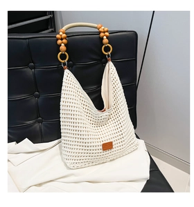 Detail of hollow knit tote bag with wooden bead handle and logo patch on black chair