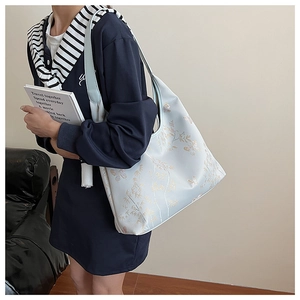 Detail of light blue tote bag with gold bamboo leaf patterns and elegant embroidery