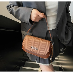 Détail d'un sac bandoulière marron tissé avec logo FASHION en métal et gland