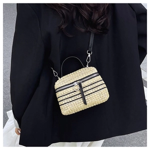 Détail du sac à bandoulière en paille tissé à la main porté sur un blazer noir