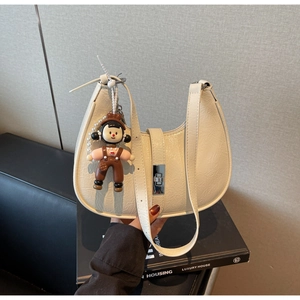 Close-up of a white pleated half-moon bag with a silver lock and cute cartoon doll charm