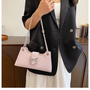 Détail d'un sac rose avec une boucle en nœud argenté et une bandoulière chaîne tressée