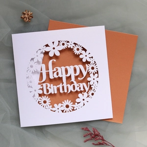 Macro shot of laser-cut floral daisy card with Happy Birthday text and bronze envelope