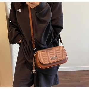 Détail d'un sac bandoulière marron avec texture tissée et logo en métal chic