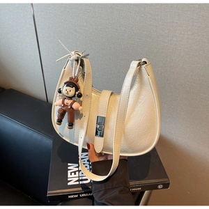 Detail of white wrinkled patent leather crescent bag with silver twist lock and doll charm