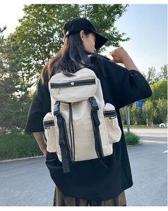 Detailed back view of a beige nylon travel backpack with black buckles on a model outdoors