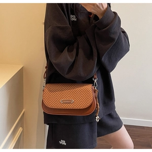Gros plan d'un sac bandoulière en cuir marron avec texture tissée en V et pompon chic