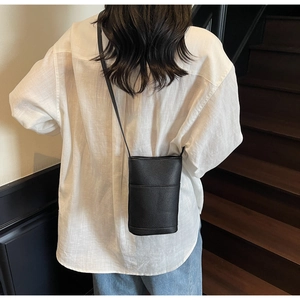 Rear view of a black pebble leather crossbody phone bag worn by a model in casual attire