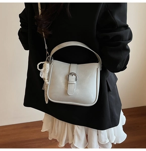 Detail of white faux leather bucket bag with silver buckle and pearl bow charm accessory