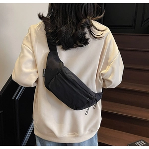 Detail of minimalist black nylon sling bag worn on back showing zipper and brand tag