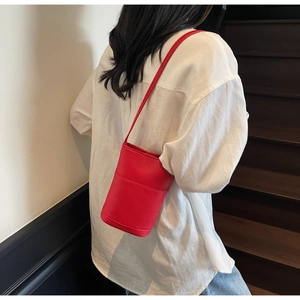 Detailed view of red bucket cross-body bag with pebble grain texture on model