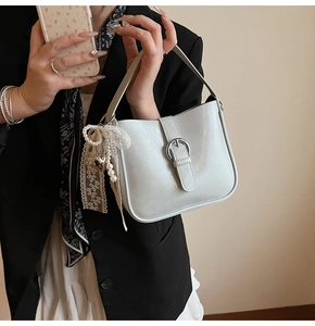 Detail of white glossy leather bag with silver metal buckle and pearl lace charm accessory