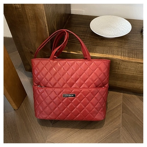 Detailed macro shot of red quilted faux leather tote bag featuring the metallic logo plaque