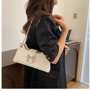 Détail d'un sac baguette blanc crème avec boucle en nœud argenté et bandoulière chaîne