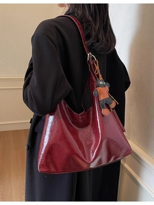 Fashionable burgundy leather tote bag with glossy finish and cat charm on shoulder