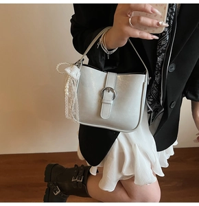 Detail of minimalist cream bucket bag with silver buckle and pearl lace charm on model