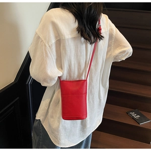 Model wearing a red pebble leather mini crossbody phone bag on a white shirt background