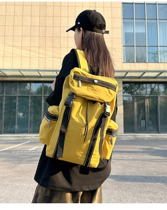 Outdoor shot of a bright yellow nylon backpack with buckle closure on model