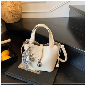 Primer plano de bolso cubo de cuero litchi blanco con dijes de perro y estrella