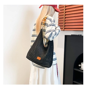 Detail of black hollow knit tote bag featuring wooden beads and orange leather patch