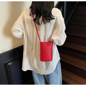 Close-up of red lychee grain leather phone bag worn by model over a white shirt