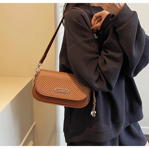 Gros plan sur un sac bandoulière marron en tissage chevrons avec rabat en cuir et plaque métal