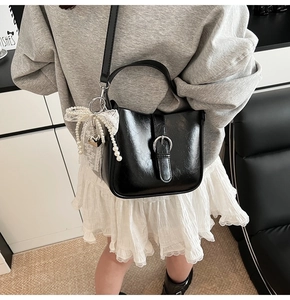 Detail view of black PU bucket bag with silver buckle and pearl bow charm accessory