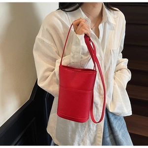 Close-up of a red leather bucket bag with litchi texture on a crossbody strap