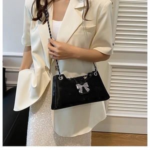 Détail du sac baguette noir brillant avec boucle nœud argenté et bandoulière chaîne