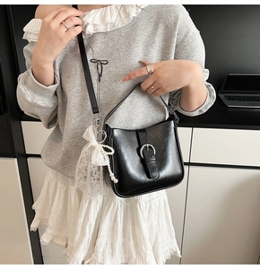 Detail of black glossy shoulder bag featuring silver ring buckle and lace pearl charms