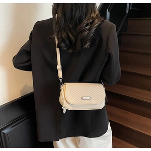 Détail d'un sac bandoulière beige à tissage chevron et plaque en métal argenté