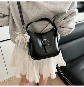 Detail of black leather shoulder bag featuring silver ring buckle and heart pearl charm