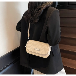 Détail du sac bandoulière tissé crème avec boucle métal sur fond de blazer noir
