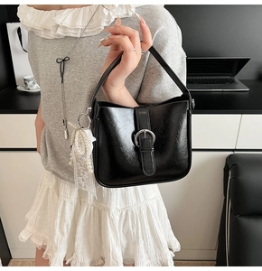 Detail of black wrinkled patent leather shoulder bag with silver buckle and pearl charm