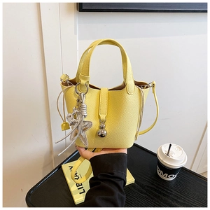 Detalle del bolso tipo cubo de cuero lichi amarillo con colgantes de estrella y bola de metal