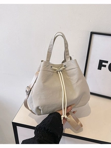 Minimalist beige nylon drawstring bucket bag with adjustable shoulder strap and handle