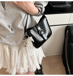 Detail of black glossy shoulder bag featuring silver buckle and elegant pearl floral charm