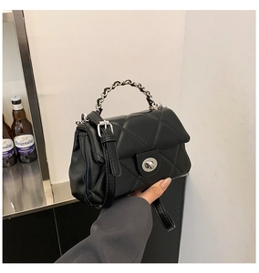 Close-up of black quilted shoulder bag featuring silver turn-lock and leather chain handle