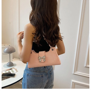 Sac baguette rose avec boucle nœud argenté porté à l'épaule par un mannequin en intérieur