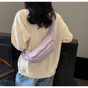Back view of a woman wearing a lavender purple nylon crossbody bag over a beige sweatshirt