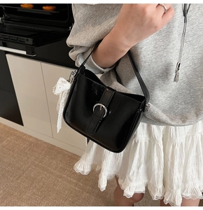 Detail of black PU leather shoulder bag with buckle and white lace bow accessory
