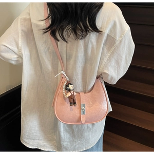 Detail of pink half-moon shoulder bag with silver metal lock and doll pendant on model